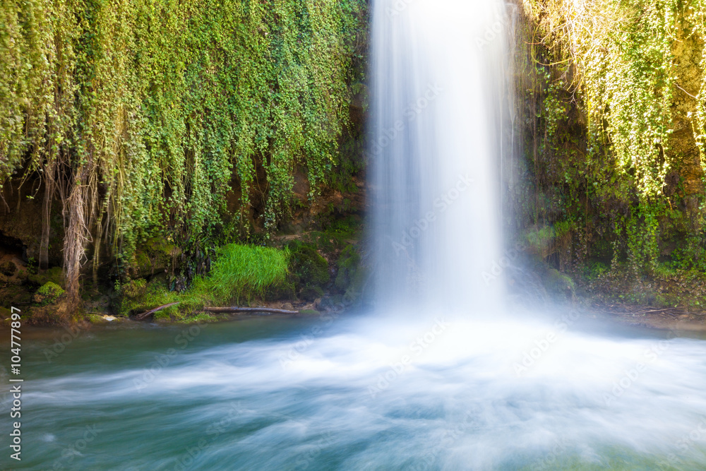 Waterfall flows between green foliage Waterfall flows between green foliage