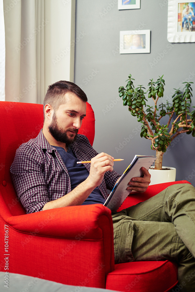young man with writing pad sitting on the chair young man with writing pad sitting on the chair