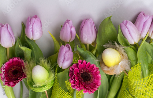Wiosenny pastelowy bukiet z liliowych tulipanów i różowych gerber na białym tle z jutową jasnozieloną taśmą ozdobną i ozdobami wielkanocnymi