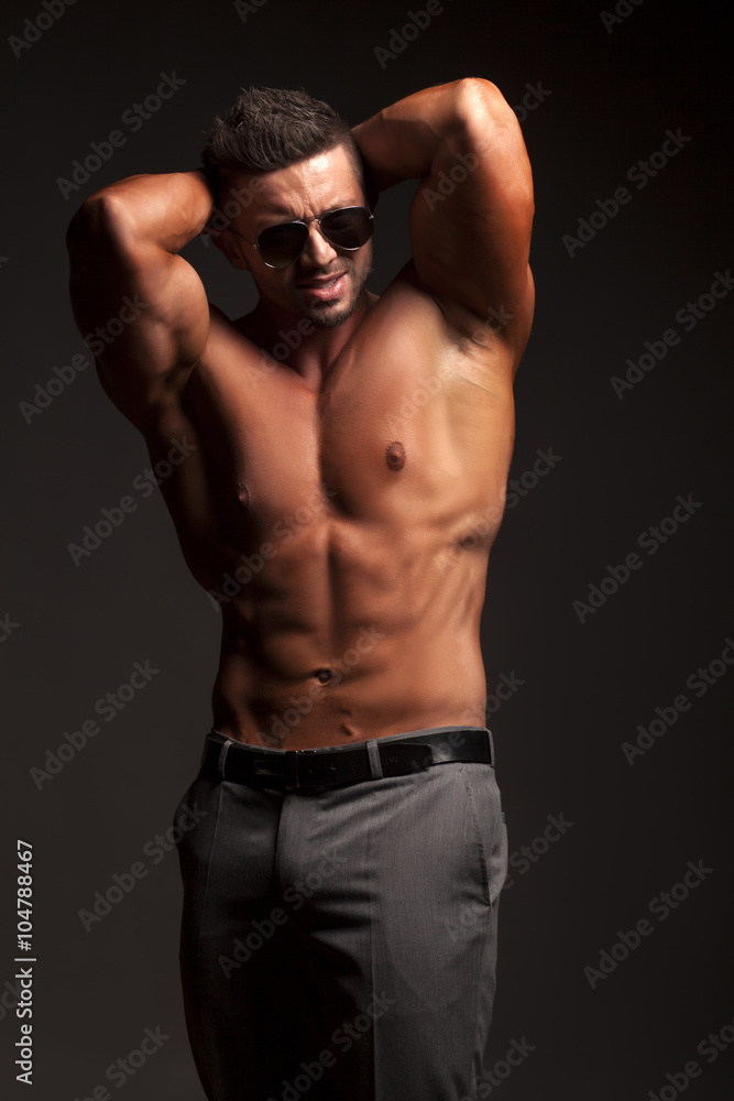 shirtless muscular man in pants and sunglasses posing in studio shirtless muscular man in pants and sunglasses posing in studio