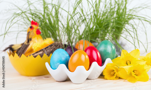 Pisanki, Wielkanocne dekoracje z kolorowymi jajami wielkanocnymi w ceramicznym stojaku, żonkilami i zielonymi roślinami w tle i kurczakiem 