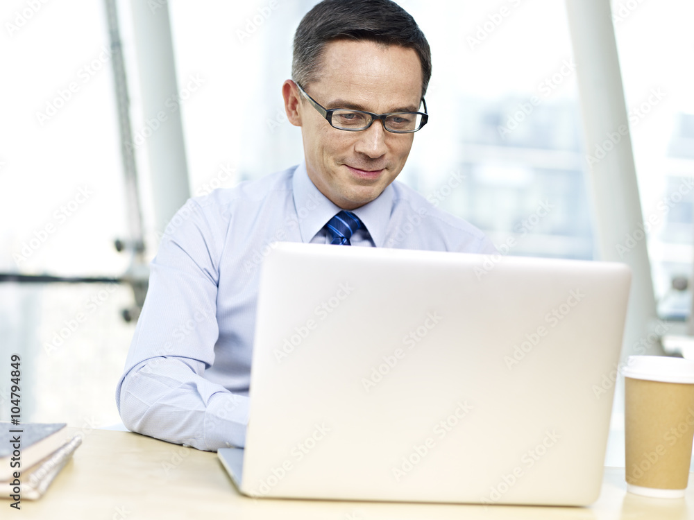 Office worker sitting at desk using laptop computer and smiling Office worker sitting at desk using laptop computer and smiling