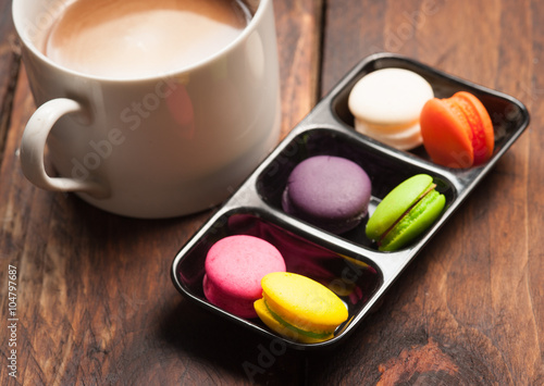 Mini macaron cookies and cup of coffee on wooden table backgroun