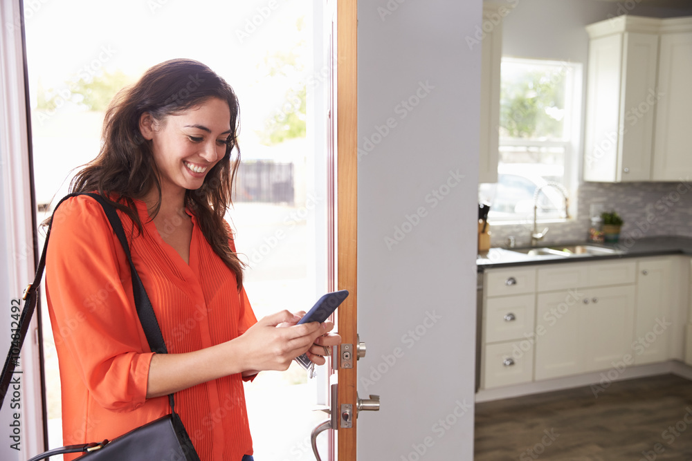 Woman Checking Mobile Phone As She Opens Door Of Apartment