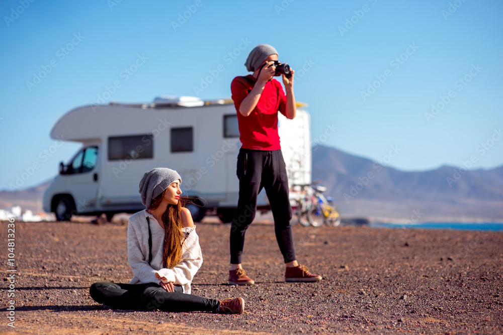 Young stylish couple having fun near the camping trailer on the deserted seaside with mountains on background on Fuerteventura island in Spain