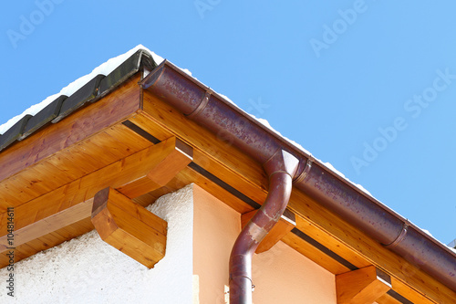 New roof top detail with ceramic tiles and copper water gutter with snow against blue skies