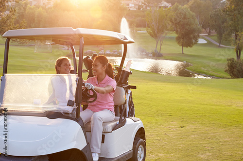 Female Golfers Driving Buggy Along Fairway Of Golf Course