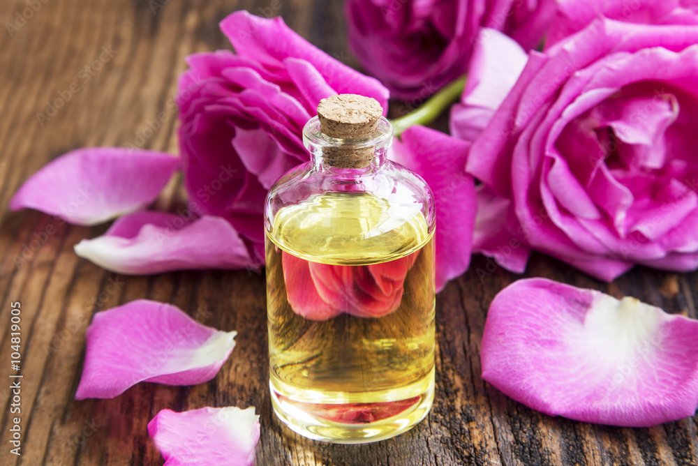 Rose essential oil with pink roses and petals on wooden board Rose essential oil with pink roses and petals on wooden board