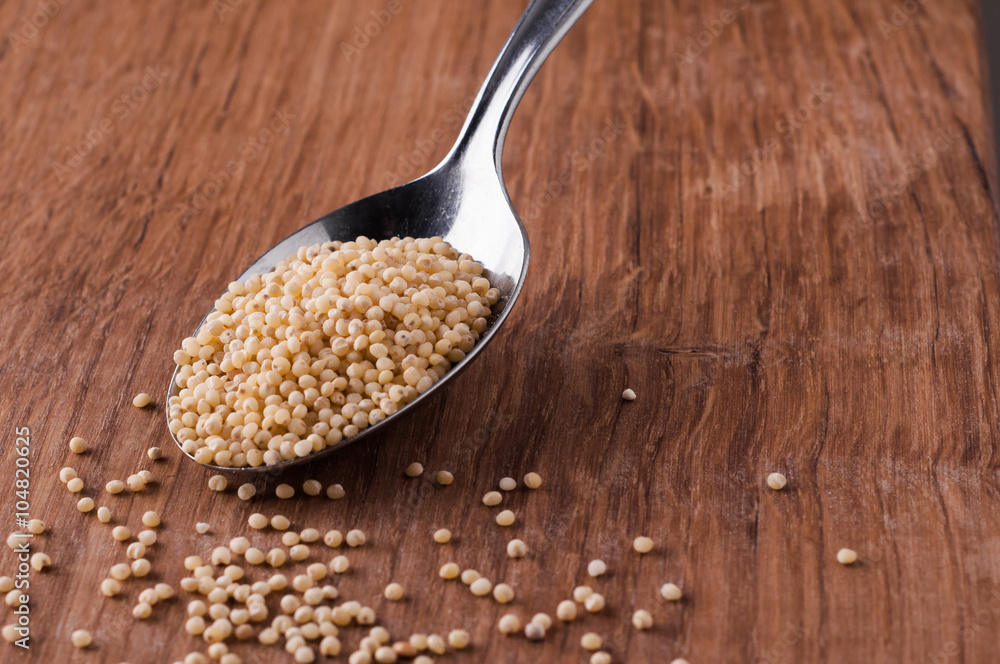 millet on metal spoon on brown wooden table millet on metal spoon on brown wooden table