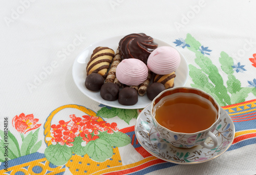 Traditional breakfast concept with colorful cup of tea  sweets and biscuits on white tablecloth with colorful print