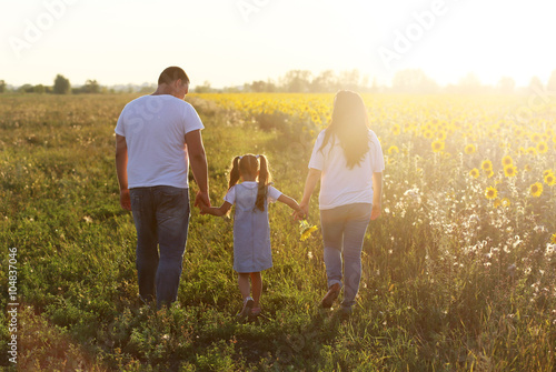 Молодая семья (муж, беременная жена, дочь) гуляют  на поляне где растут подсолнухи в светлый яркий солнечный день