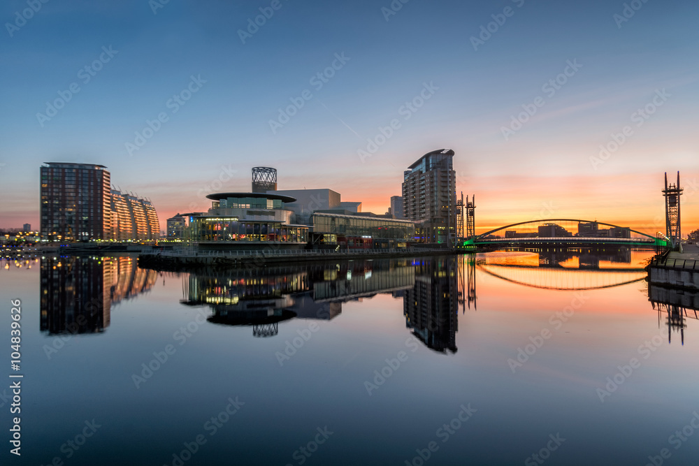 Orange sunrise at Salford Quays with blue sky and clear reflections in canal. - obrazy, fototapety, plakaty 
