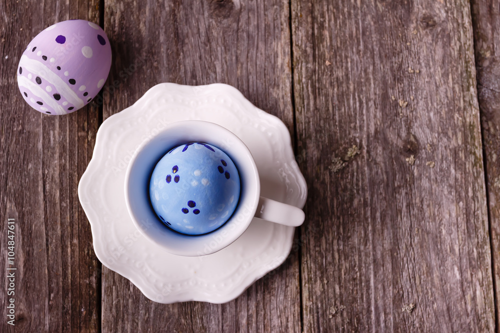 Easter painted blue egg in white cup on wooden rustic background. Empty space for text. Easter painted blue egg in white cup on wooden rustic background. Empty space for text.