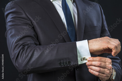 Elegant businessman correcting his cufflinks and sleeve. © pavel_shishkin