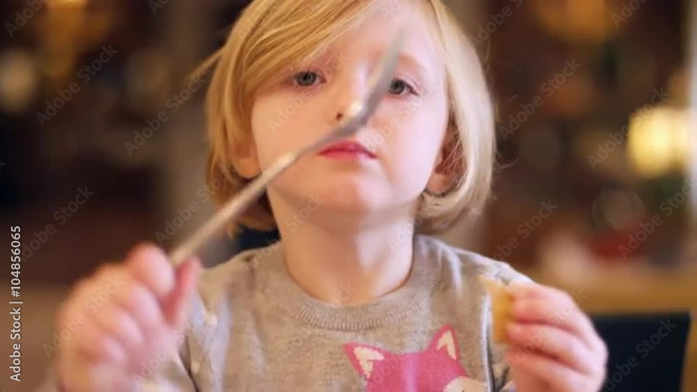 A little girl sitting in the kitchen with bokeh behind her, holding a fork up and eating crackers, slow motion A little girl sitting in the kitchen with bokeh behind her, holding a fork up and eating crackers, slow motion