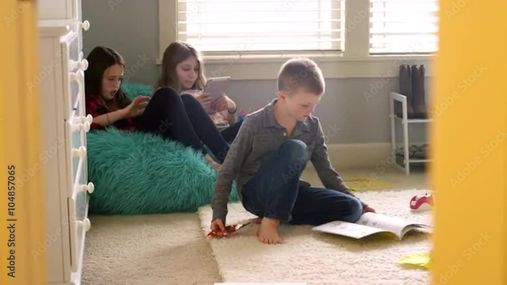 Three kids playing at home with tablets and origami, door frame in the foreground Three kids playing at home with tablets and origami, door frame in the foreground