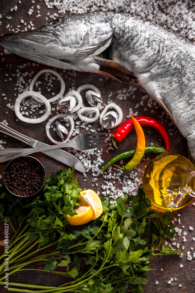 Delicious fresh fish with aromatic herbs, spices and vegetables on dark vintage background
