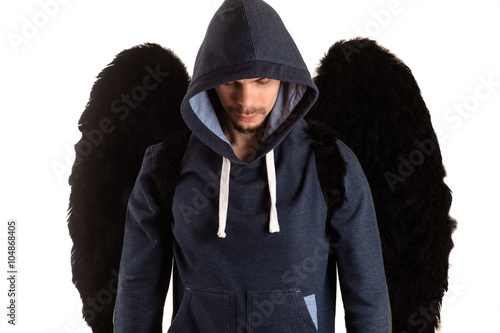 young man in gray jacket with hood thrown over his head standing with her hands and looks down on his back and black wings
