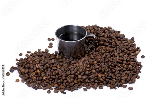 the steel cup of coffee surrounded with coffee grains