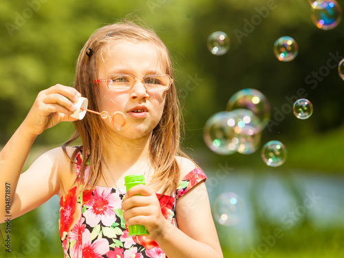 Little girl child blowing soap bubbles outdoor.
