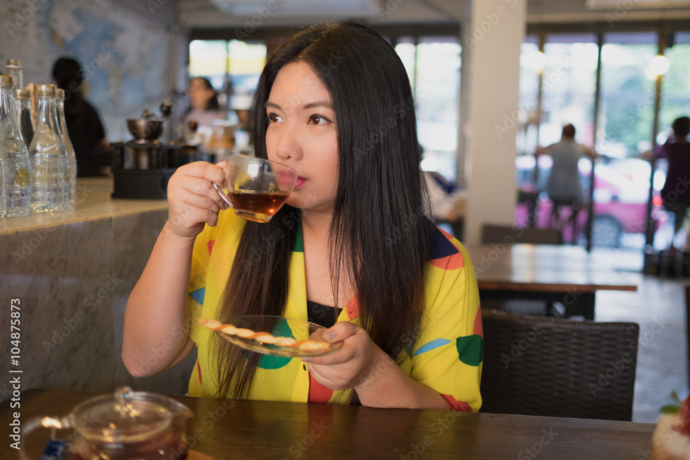 Woman is drinking hot tea /Woman in colorful dress is drinking and sipping hot tea in coffee shop Woman is drinking hot tea /Woman in colorful dress is drinking and sipping hot tea in coffee shop