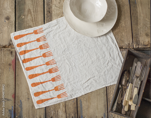 White Napkin with Orange Fork Pattern Alongside Flatware and Tra photo