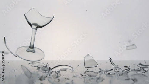 SLOW: A clear winegalss falls and breaks on a white table
