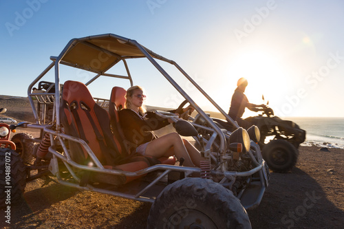 Fotografia Active woman driving quadbike on dirt road by the sea in sunset.
