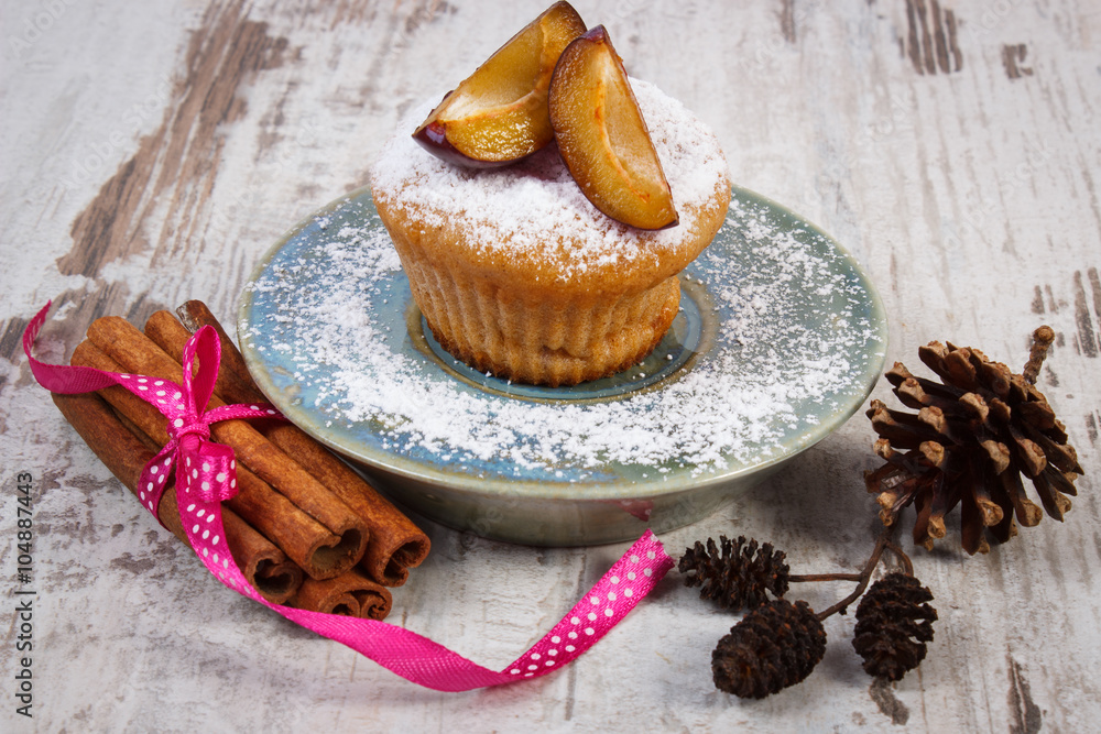 Muffins with plums and powdered sugar, cinnamon sticks on old wooden background, delicious dessert