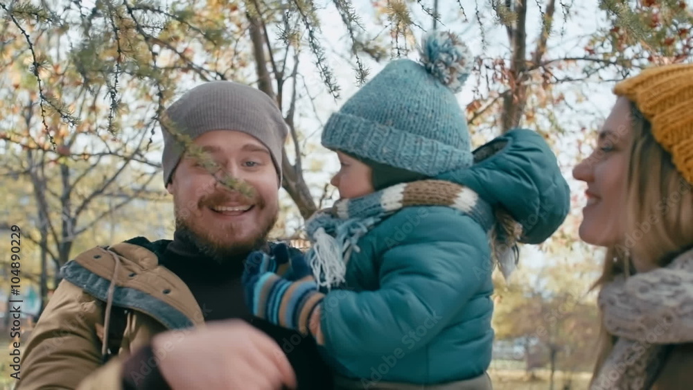 Daddy holding cute little son on his arms and playing with tree branch in the park while their mom standing next to them and smiling Daddy holding cute little son on his arms and playing with tree branch in the park while their mom standing next to them and smiling