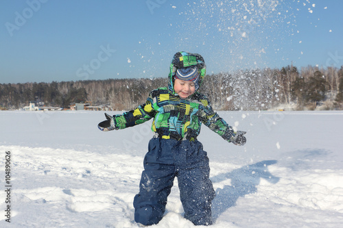 The little boy in a color jacket with a hood throws snow during a winter entertainment up 