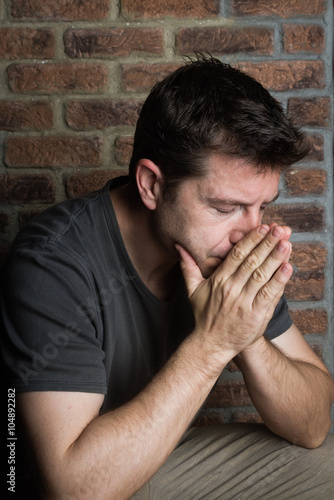 Middle-age man with palms raised to face and eyes closed