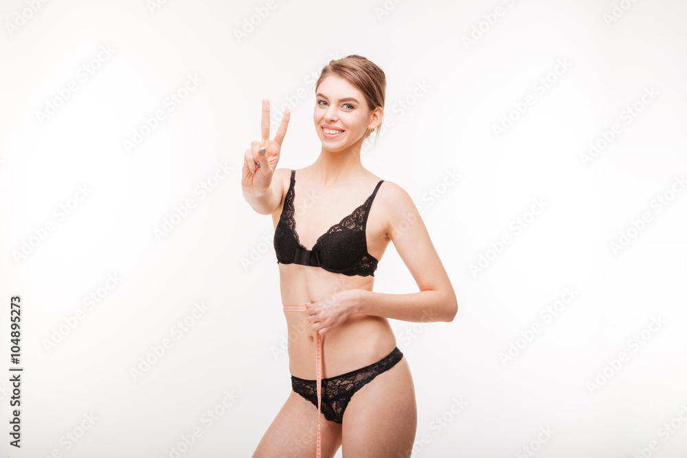 Cheerful woman showing victory sign and measuring her waist Cheerful woman showing victory sign and measuring her waist