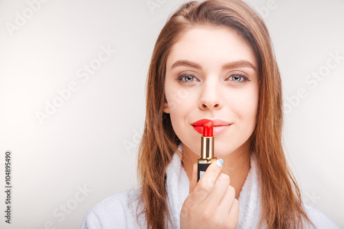 Beautiful smiling young woman in bathrobe using red lipstick
