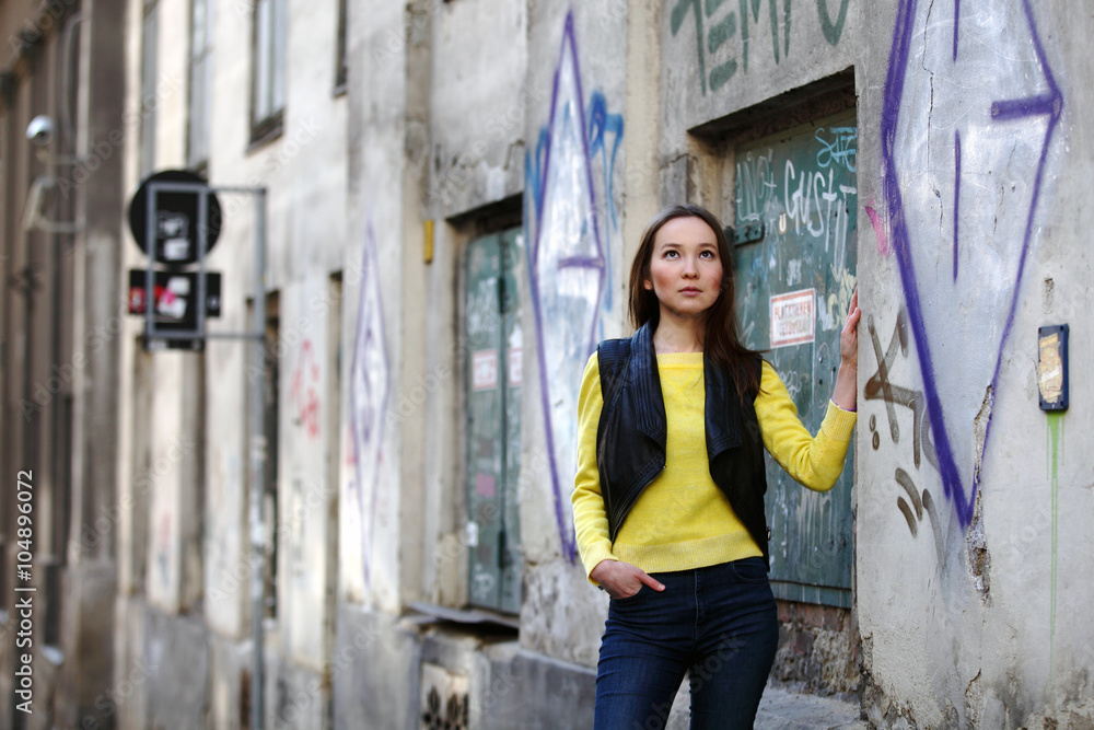 Beautiful Asian woman in yellow sweater and jeans standing at a house with graffiti