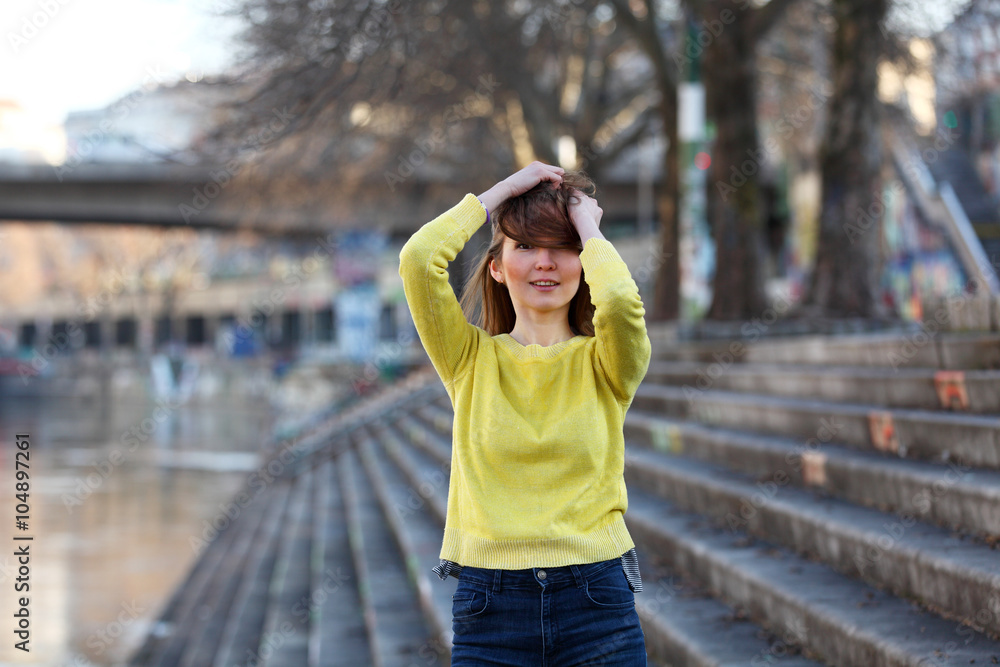 Beautiful Asian woman in yellow sweater standing at a river in a European city