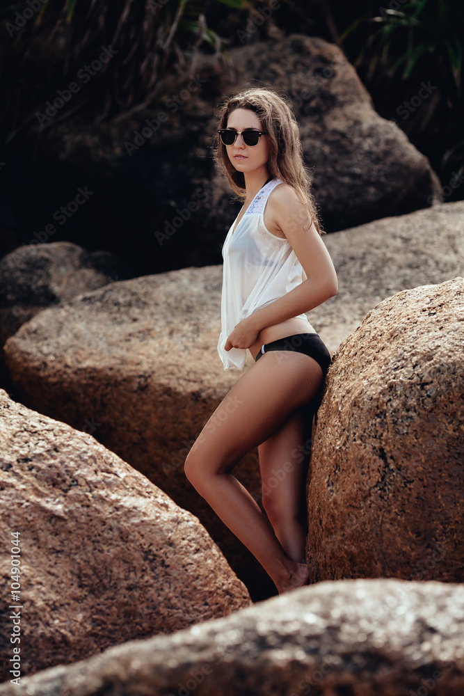 Young girl in black swimsuit and white bluse on the rocks near t