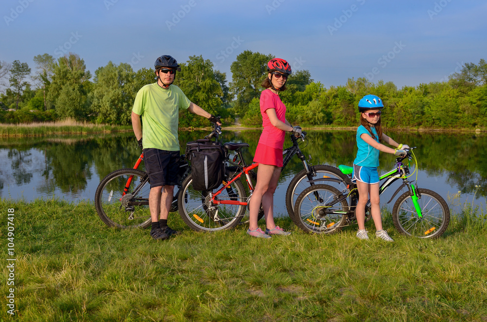 Family bikes ride outdoors, active happy parents and kid cycling and relaxing near beautiful river
