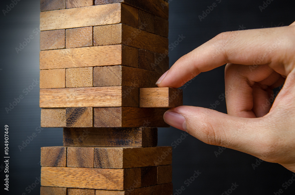Closeup hand man take one block on The tower from wooden blocks, dark tone. Closeup hand man take one block on The tower from wooden blocks, dark tone.
