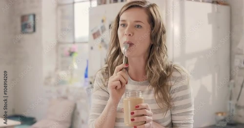 Caucasian girl indulging eating peanut butter from jar using spoon at home in the morning Caucasian girl indulging eating peanut butter from jar using spoon at home in the morning