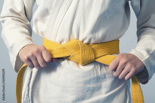 Hands tightening yellow belt on a teenage dressed in kimono for martial arts