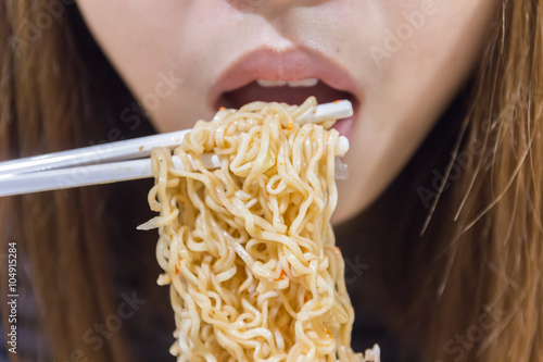 Noodle on chopsticks with people in background, shallow depth of