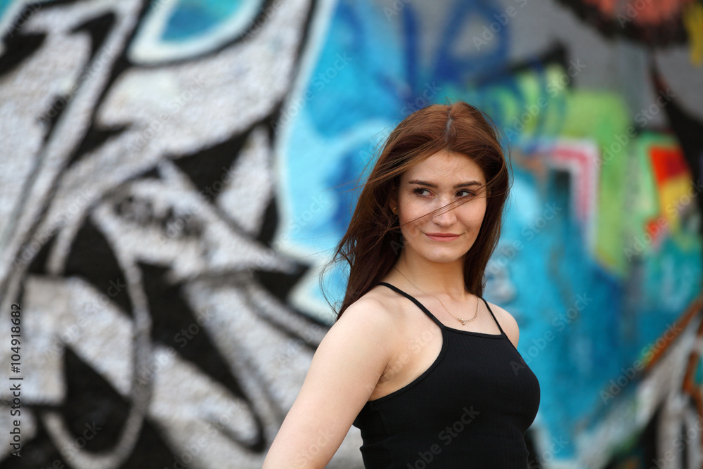 Naklejka premium Beautiful girl with red hair standing in front of a wall with graffiti