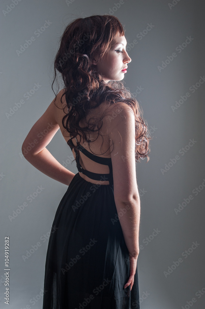 Fototapeta premium Young lady standing with a long black dress and long curly hair 