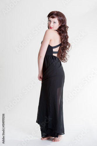 Young lady standing with a long black dress and long curly hair 