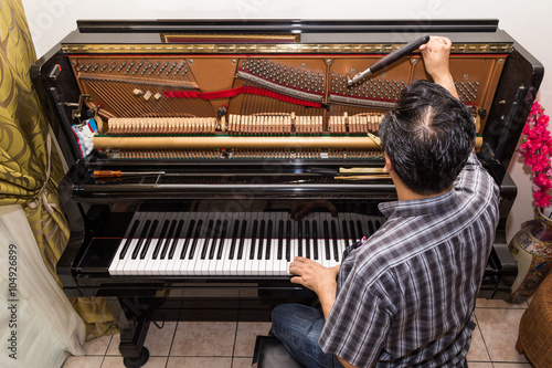 Technician tuning a upright piano using lever and tools
