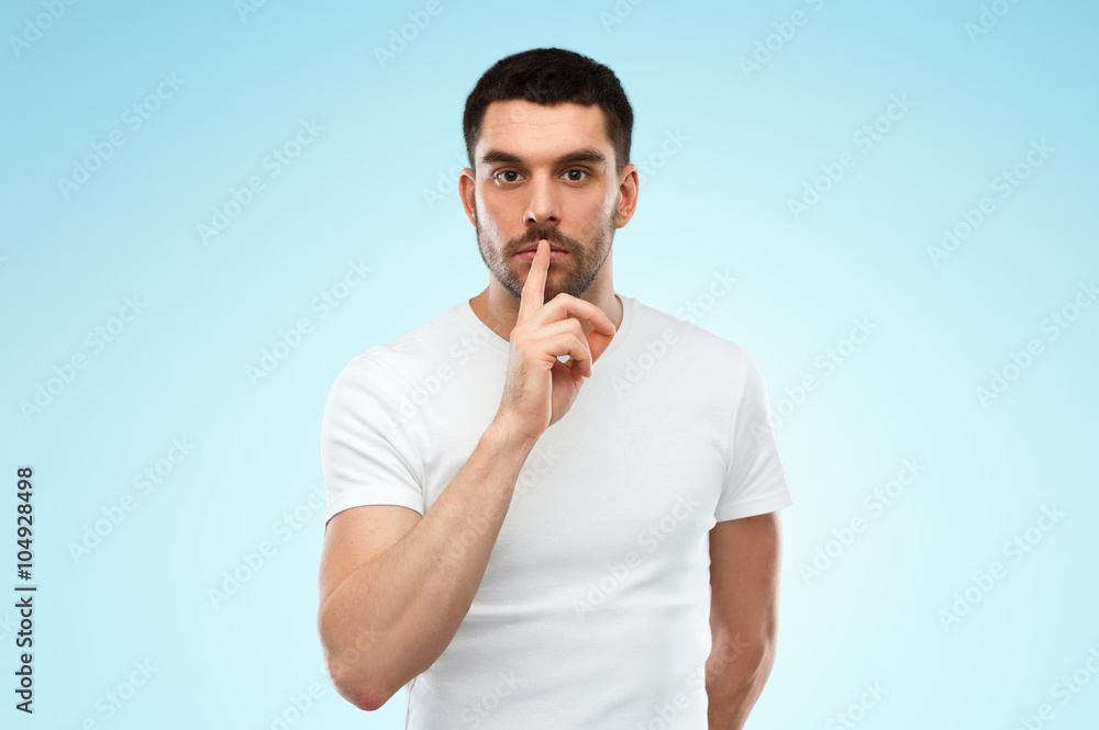 young man making hush sign over blue background young man making hush sign over blue background