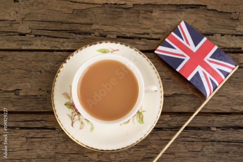 A cup of tea in a bone china cup and saucer with a union jack flag on a rough wooden table