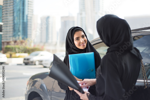 Two Middle Eastern Emirati Businesswomen Discuss Something next to a Car