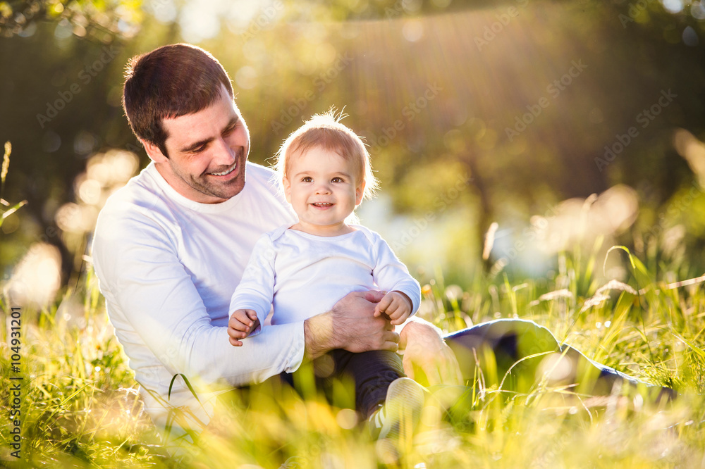 Fototapeta premium Father holding his little son, sitting on the grass